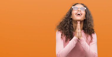 Güzel genç İspanyol kadın yalvarıyor ve umut ifade yüzünde çok duygusal ve endişe ile birlikte elleriyle dua güneş gözlüğü takıyor. Bağışlanmak. Din kavramı.