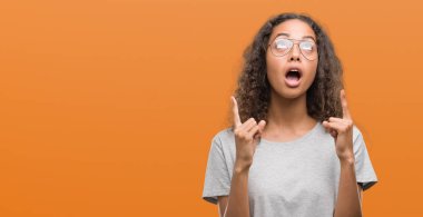 Güzel genç İspanyol kadın gözlük takan hayrete ve yukarıya bakıyor ve parmakları ile işaret ve silah kaldırdı şaşırttı.