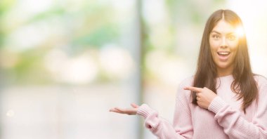 Hayret ve el ile sunulması ve parmak ile işaret ederken kameraya gülümseyen bir kazak giyen genç güzel İspanyol kadın.