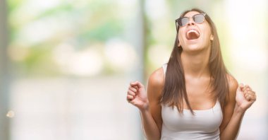 Silah ile başarı için heyecanlı güneş gözlüğü takmış genç güzel İspanyol zafer kutluyor gülümseyen kaldırdı. Kazanan kavramı.