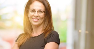 Orta yaş kadın siyah gömlek ve kendinden emin ve mutlu bir büyük doğal gülümseme gülmek ile çapraz kollu gözlük