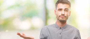 Genç hipster adam clueless ve şaşkın bir ifadeyle kollar ve eller kaldırdı. Şüphe kavramı.