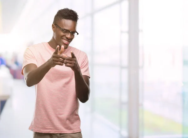 若いアフリカ系アメリカ人の幸せと面白い顔でカメラにピンク シャツ指を指してを身に着けています 良いエネルギーとヴァイブス — ストック写真