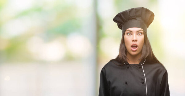 Young hispanic cook woman wearing chef uniform scared in shock with a surprise face, afraid and excited with fear expression