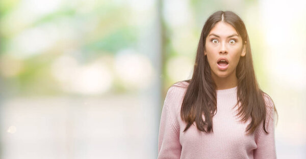 Young beautiful hispanic woman wearing a sweater afraid and shocked with surprise expression, fear and excited face.