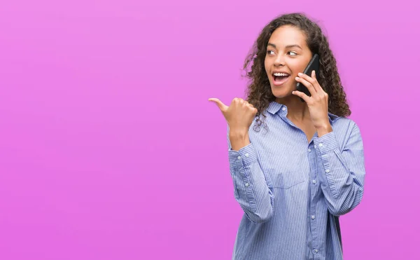 年轻的西班牙裔妇女使用智能手机指向和显示与拇指到一边 快乐的脸微笑 — 图库照片