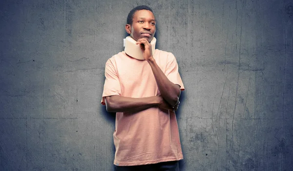 Injured african black man wearing neck brace thinking and looking up expressing doubt and wonder