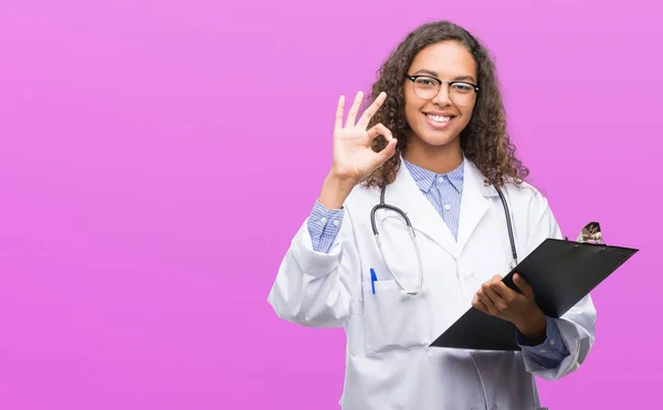 優秀なシンボルの指で サインをしているクリップボードを保持している若いヒスパニック医師女性 — ストック写真