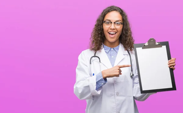 Joven Doctora Hispana Sosteniendo Portapapeles Muy Feliz Señalando Con Mano —  Fotos de Stock