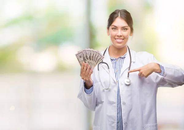 Jovem Hispânico Médico Mulher Segurando Dólares Com Rosto Surpresa Apontando — Fotografia de Stock