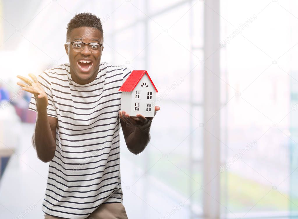 Young african american man holding house very happy and excited, winner expression celebrating victory screaming with big smile and raised hands