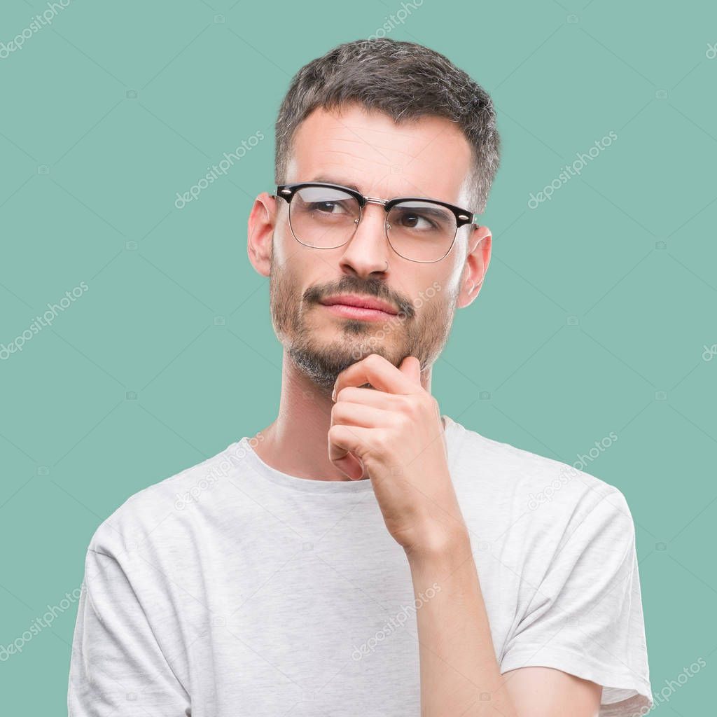 Young tattooed adult man with hand on chin thinking about question, pensive expression. Smiling with thoughtful face. Doubt concept.