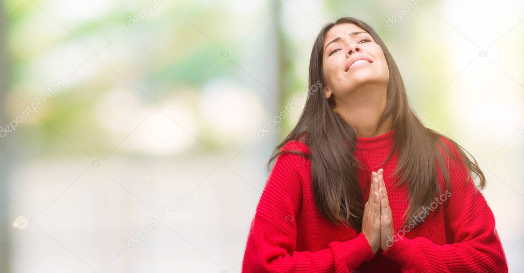 Young beautiful hispanic wearing red sweater begging and praying with hands together with hope expression on face very emotional and worried. Asking for forgiveness. Religion concept.