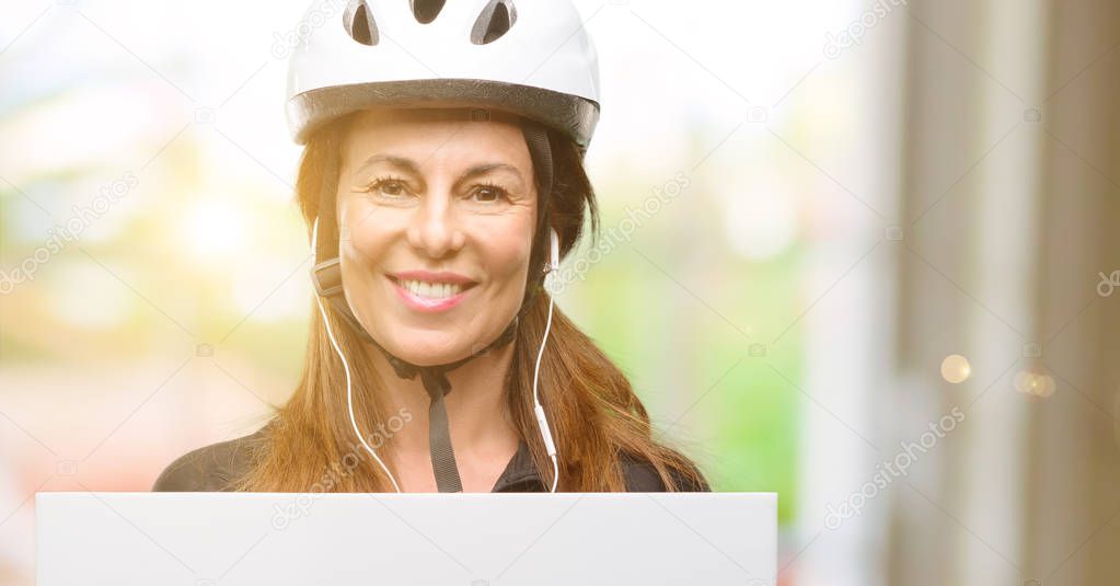 Middle age cyclist woman using earphones holding blank advertising banner, good poster for ad, offer or announcement, big paper billboard