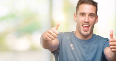 Yakışıklı genç casual adam el ile pozitif jest yapıyor onaylama başparmak gülümseyen ve başarı için mutlu. Kamera, kazanan jest arıyorsunuz.