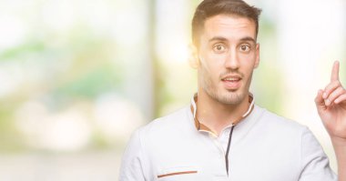 Yakışıklı genç casual adam beyaz t-shirt bir fikir ya da soru işaret parmağı gülen yüz, bir numara ile sürpriz giyiyor