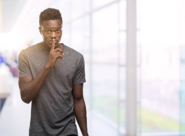 Dudaklarında parmak ile sessiz olmanı gri t-shirt giyen genç Afro-Amerikan adam. Sessizlik ve gizli kavramı.