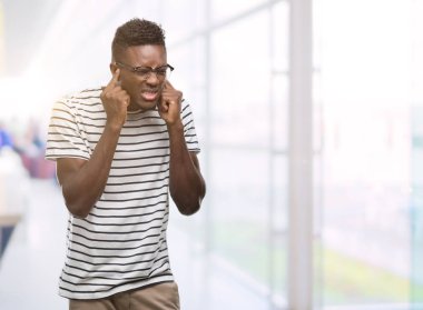 Gözlük ve lacivert t-shirt kapsayan kulakları ile parmak yüksek sesle müzik gürültü rahatsız ifade ile giyen genç Afro-Amerikan adam. Sağır kavramı.