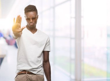 Afro-Amerikan delikanlı açık eliyle dur işareti ile ciddi ve kendine güvenen ifade, savunma hareketi yaparken güneş gözlüğü takıyor