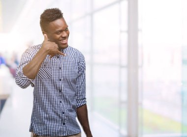 Mavi gömlek gülümseyen giyen genç Afro-Amerikan adam el ve parmak telefonda konuşmak ile telefon jest yapıyor. Kavramları iletişim.