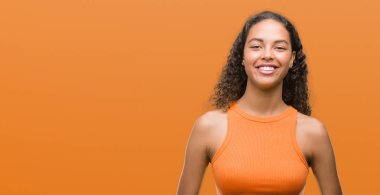 Ayakta ve diş gösterilen kendine güvenen bir gülümsemeyle gülümseyerek mutlu bir yüz olan İspanyol kadın