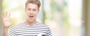 Genç yakışıklı sarışın adam büyük gülümseme ile çığlık zaferini kutluyor ve ellerini kaldırdı futbol topu çok mutlu ve heyecanlı, kazanan ifade holding