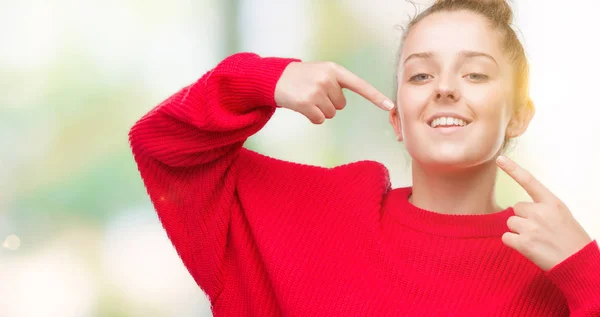 お団子と自信を示すと指歯と口を指して笑って赤いセーターを身に着けている若いブロンドの女性 健康の概念 — ストック写真