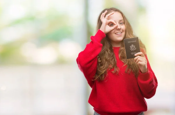 Young blonde woman holding passport of United States of America with happy face smiling doing ok sign with hand on eye looking through fingers