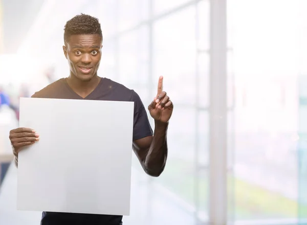 Young African American Man Holding Banner Surprised Idea Question Pointing — Stock Photo, Image