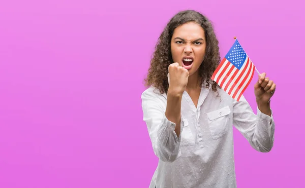 Young hispanic woman holding flag of United Estates of America annoyed and frustrated shouting with anger, crazy and yelling with raised hand, anger concept