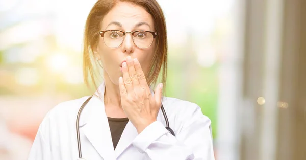 Doctor woman, medical professional covers mouth in shock, looks shy, expressing silence and mistake concepts, scared