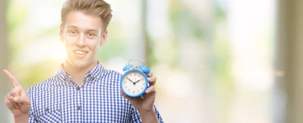 Jovem Homem Loiro Bonito Segurando Despertador Muito Feliz Apontando Com — Fotografia de Stock