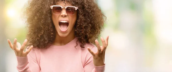 アフリカ系アメリカ人女性の狂気と叫ぶと積極的な表現と腕を上げると叫んで怒ってピンクのサングラスをかけています 欲求不満のコンセプト — ストック写真