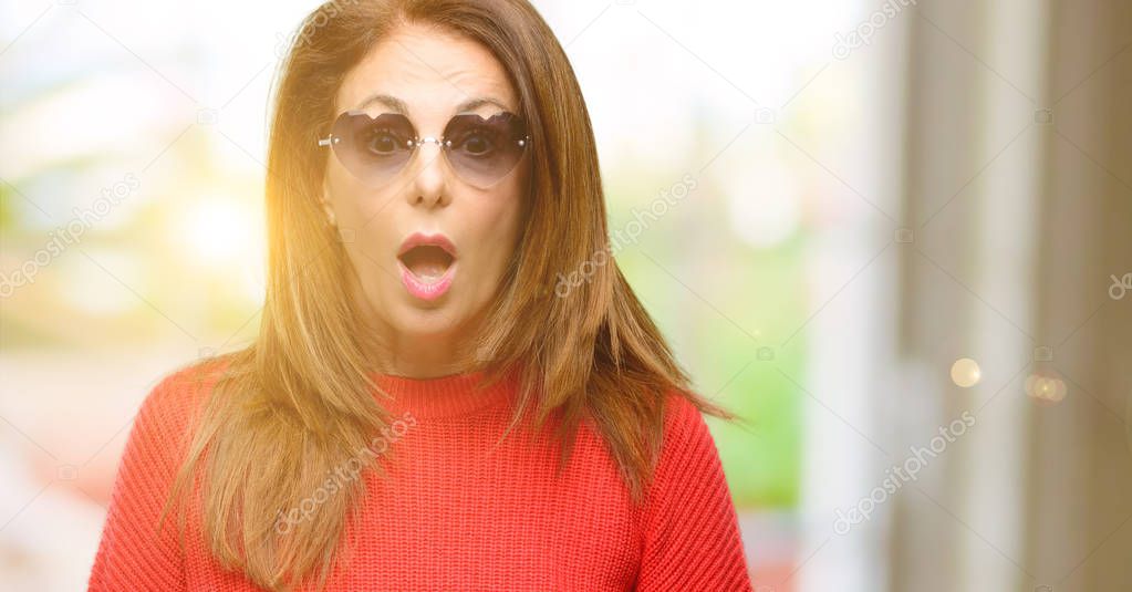 Middle age woman wearing heart sunglasses scared in shock, expressing panic and fear