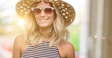 Genç kadın güneş gözlüğü yaz şapka kendinden emin ve mutlu bir büyük doğal gülümseme gülmek ile kullanma