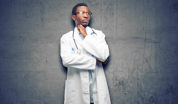 Young black doctor, medical professional thinking and looking up expressing doubt and wonder
