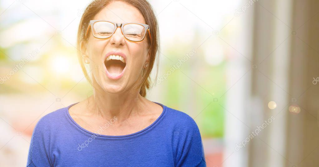 Middle age woman wearing wool sweater and glasses stressful, terrified in panic, shouting exasperated and frustrated. Unpleasant gesture. Annoying work drives me crazy