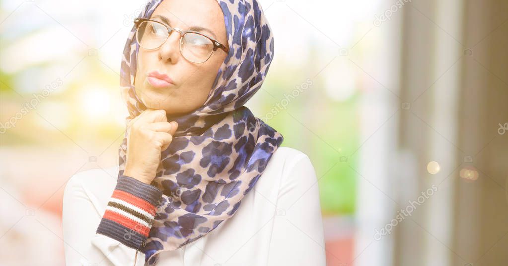 Middle age muslim arab woman wearing hijab thinking and looking up expressing doubt and wonder