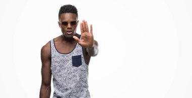 Afro-Amerikan delikanlı açık eliyle dur işareti ile ciddi ve kendine güvenen ifade, savunma hareketi yaparken güneş gözlüğü takıyor