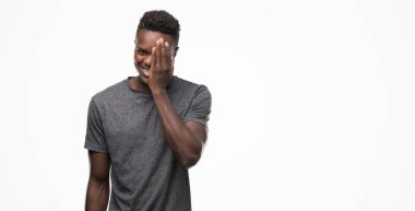 El yüz ve sürpriz duygu kendinden emin gülümseme ile tek gözü kaplayan gri t-shirt giyen genç Afro-Amerikan adam.