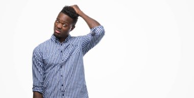 Young african american man wearing blue shirt confuse and wonder about question. Uncertain with doubt, thinking with hand on head. Pensive concept. clipart