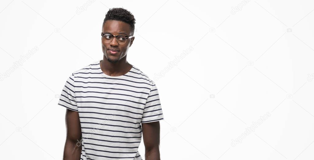 Young african american man wearing glasses and navy t-shirt smiling looking side and staring away thinking.