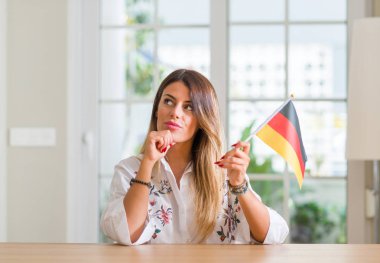 Young woman at home holding flag of Germany serious face thinking about question, very confused idea clipart