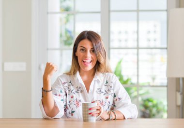 Duygu tezahürat genç kadın ev gurur çığlık kahve içme ve zafer ve başarı çok heyecanlı, kutluyor