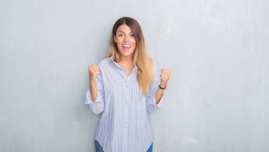 Genç Yetişkin kadın moda iş kutluyor kıyafet giyen gri grunge duvarın üzerinden şaşırttı ve başarı için kaldırdı kollarını açarak hayret ve gözleri açık. Kazanan kavramı.