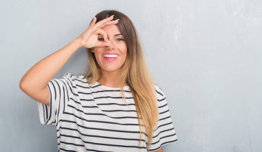 Grunge Genç Yetişkin kadın gri gülümseyen, parmakları ile mutlu yüz üzerinden seyir göz el ile ok jest yapıyor lacivert t-shirt giyen duvar.