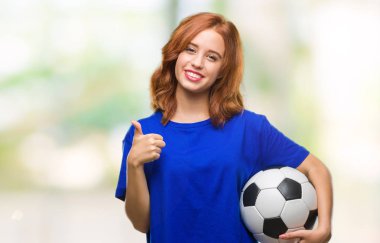 Genç güzel kadın futbol futbol topu ok işareti, başparmak ile parmak, mükemmel işareti yapıyor kocaman bir gülümseme ile mutlu tutarak izole arka plan üzerinde