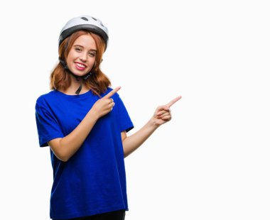 Gülümseyen ve iki elleri ve parmakları ile tarafına işaret kamera bakarak izole arka plan üzerinde bisikletçi kask giyen genç güzel kadın.