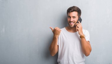 İşaret ve başparmak kadar mutlu yüz gülümseyen tarafı ile gösterilen telefonda konuşan gri grunge duvarın üzerinden yakışıklı genç
