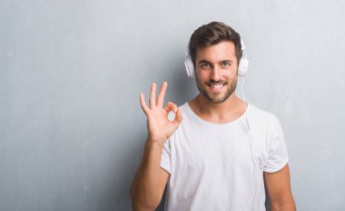Parmak, mükemmel sembolü ile ok işareti yaparken müzik dinlemek kulaklıklar giyen gri grunge duvarın üzerinden yakışıklı genç